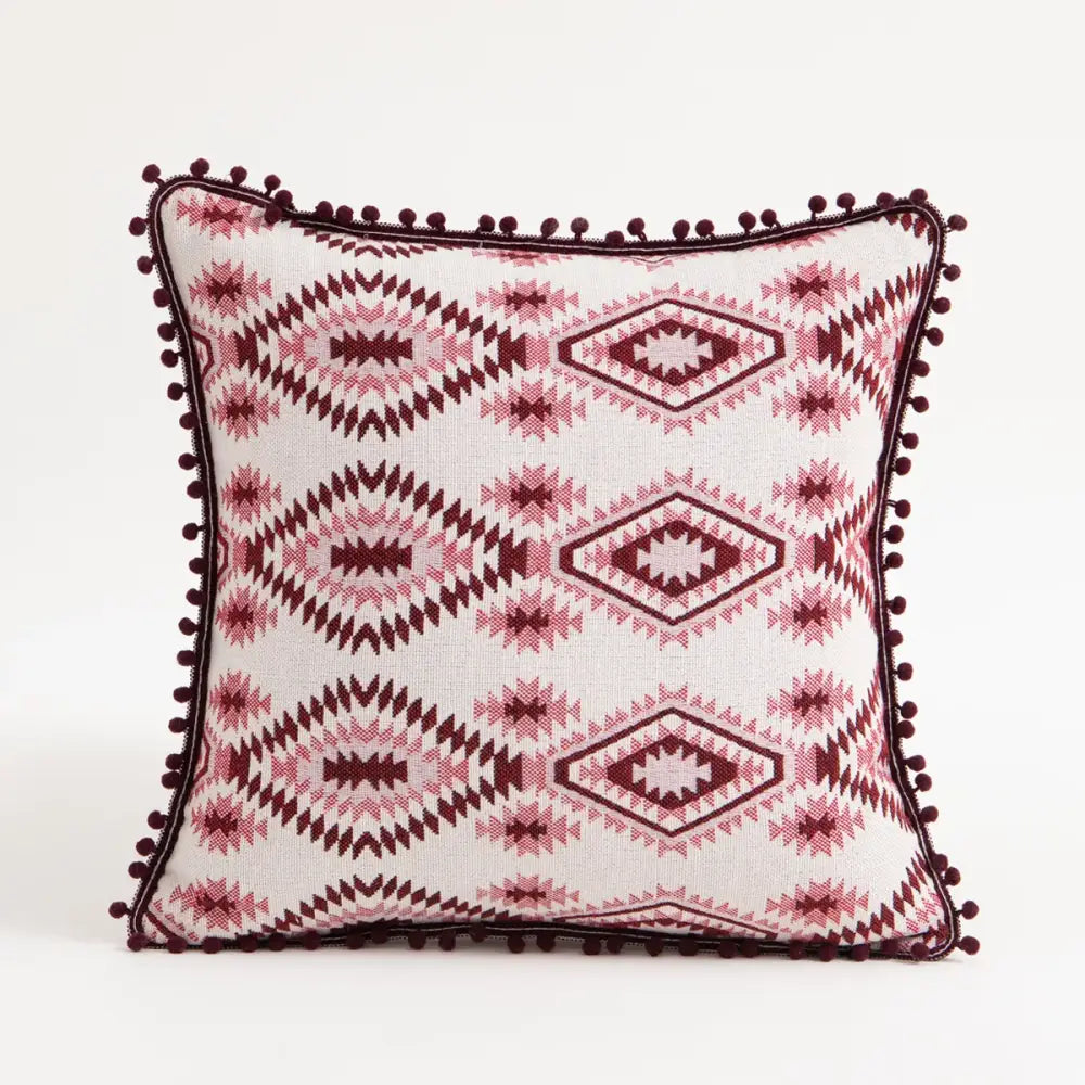 A vibrant ethnic boho throw pillow cover with white base pink maroon geometric patterns and dark red pom-pom trim decorbites