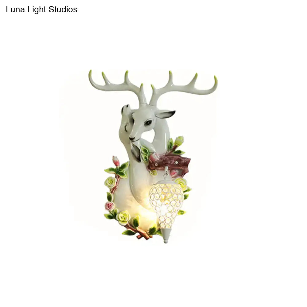 A white ceramic deer head accent wall sconce with antlers, floral wreath, and a glowing lattice-style bulb for bedroom light