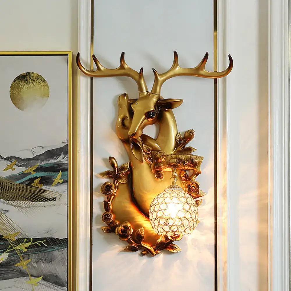 Golden deer head accent wall sconce with ornate antlers, floral detailing, and crystal globe light for bedroom use