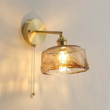 A warm amber glass copper led wall lamp with textured design and brass finish for bedroom use with pull chain