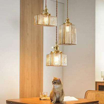 Three brass-finished vintage amber glass pendant lights with textured shades hanging from twisted cords for dining room