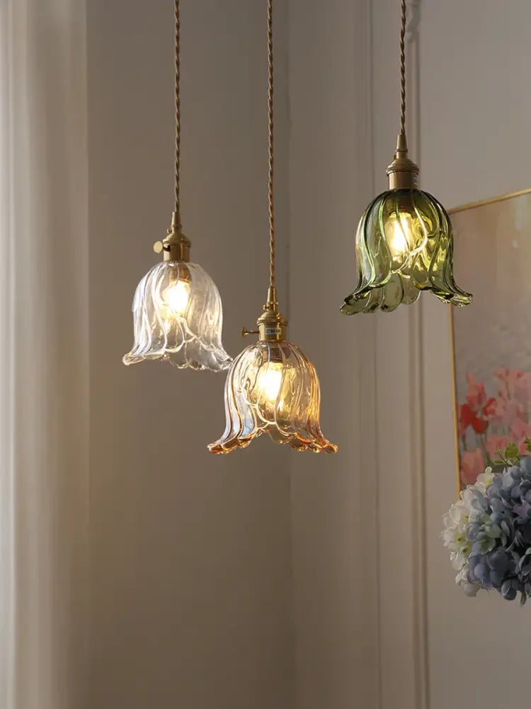Three hanging amber glass pendant lights with bell-shaped shades and twisted brass cords for kitchen island lighting