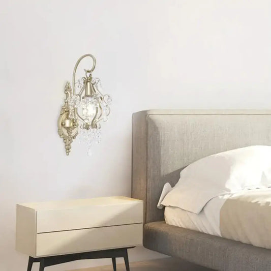 Antique brass wall lamp with clear crystal beaded strand and ornate curved design for elegant bedroom lighting