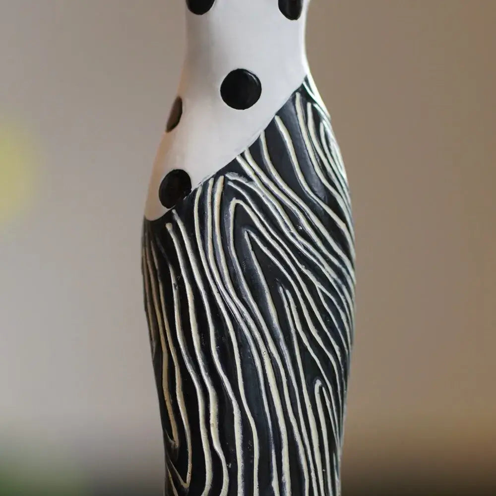 A tall ceramic vase with white polka dots and black wavy stripes complementing african women resin decorbites decor