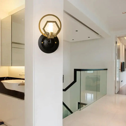 Gold-toned hexagonal wall lamp with black circular base and brass accents for living space with black finish