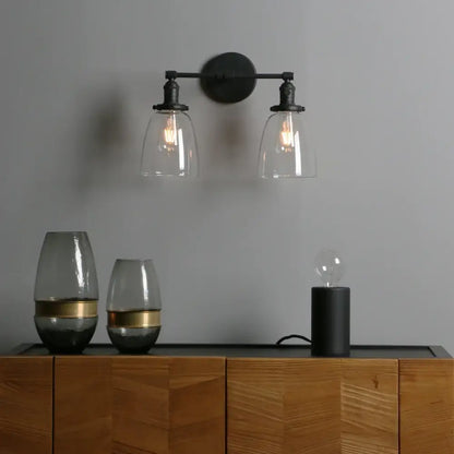 Vintage black wrought iron wall sconce with two clear glass shades and exposed filament bulbs for bedroom lighting