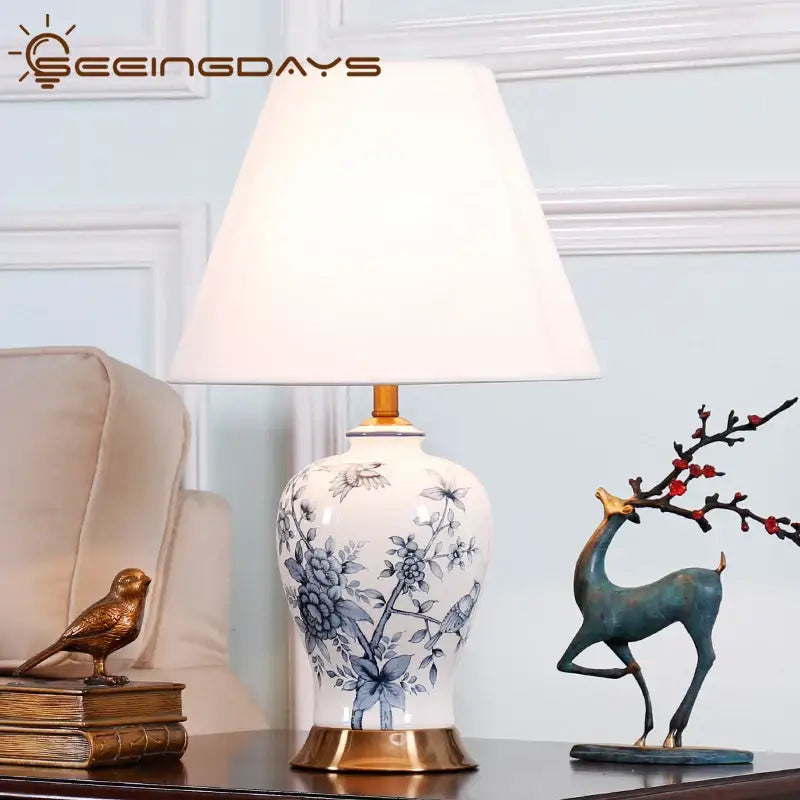 Vintage blue and white porcelain table lamp with white ceramic body, blue floral and bird designs, gold-toned base for decorbites