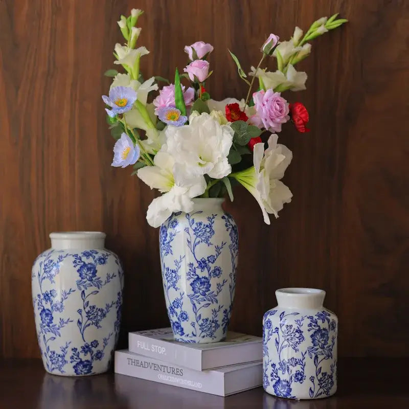 A tall blue white porcelain vase with intricate floral patterns from decorbites holds a vibrant mixed flower bouquet