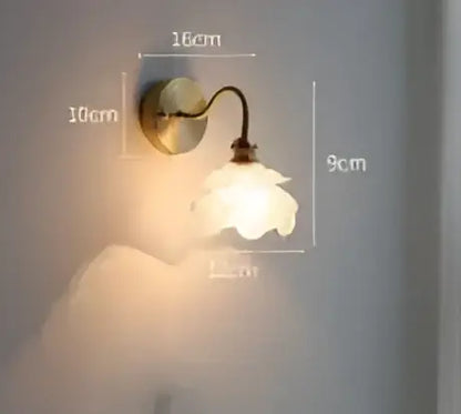 Vintage brass and amber glass led wall lamp featuring a delicate curved arm and white ceramic flower shade for bedroom use