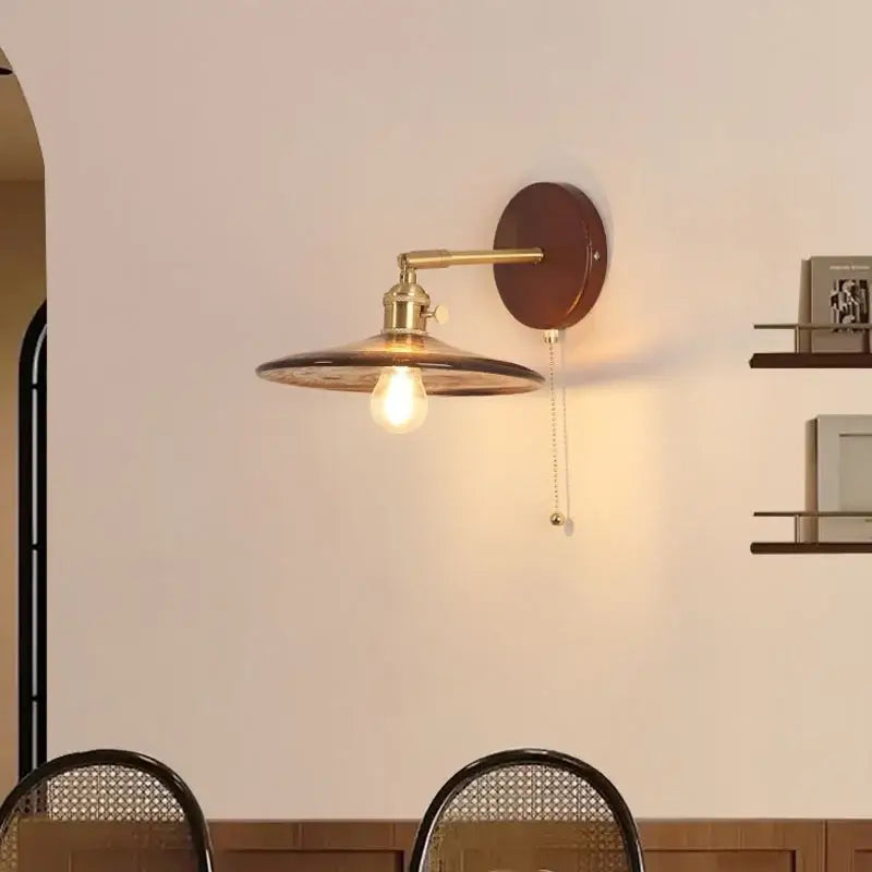 Vintage brass wall sconce with amber glass shade and pull chain switch on dark brown wooden backplate