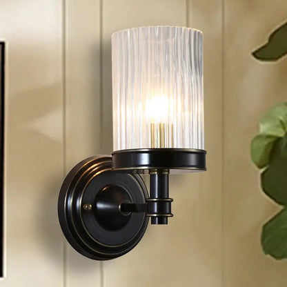 Vintage brass and black wall lamp with clear ribbed glass cylinder shade for bedroom lighting