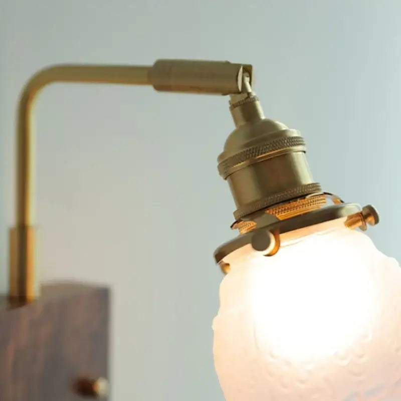 Brass-finished adjustable arm wall sconce with frosted glass pink led globe for bedroom bedside lighting