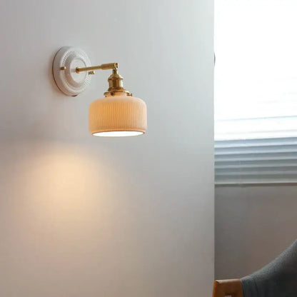Vintage brass globe wall sconce with cream-colored ribbed glass and brass hardware mounted on a white wall plate
