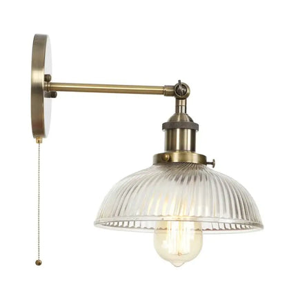 Vintage brass wall sconce with ribbed glass shade and pull chain switch featuring an exposed filament bulb