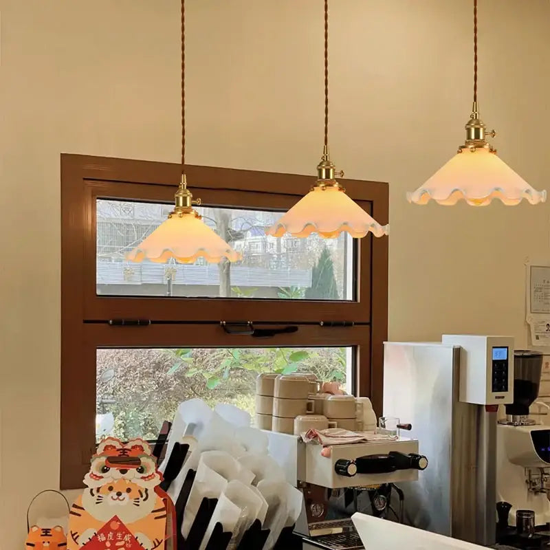 Two vintage brass pendant lights with scalloped off-white glass led shades hanging from braided cords for bedroom lighting