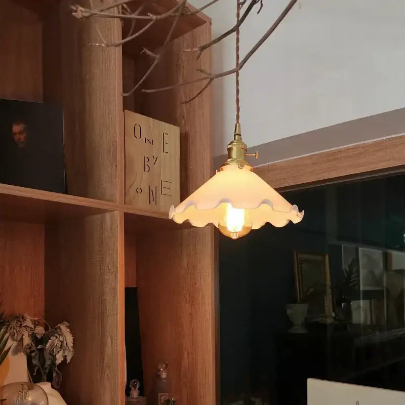 A warm cream-colored glass led pendant lamp with scalloped edge and brass hardware suitable for bedroom lighting