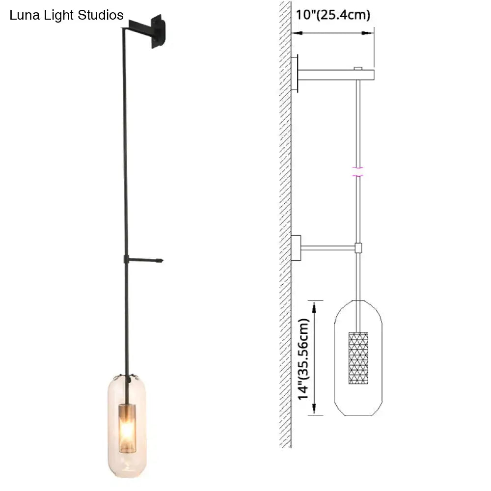 Black metal wall sconce with a brass wall lamp design and a clear glass cylinder shade housing an illuminated bulb
