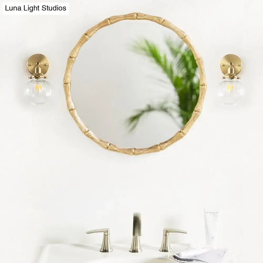 Round mirror with bamboo-inspired gold frame paired with vintage brass wall light featuring champagne clear glass shade