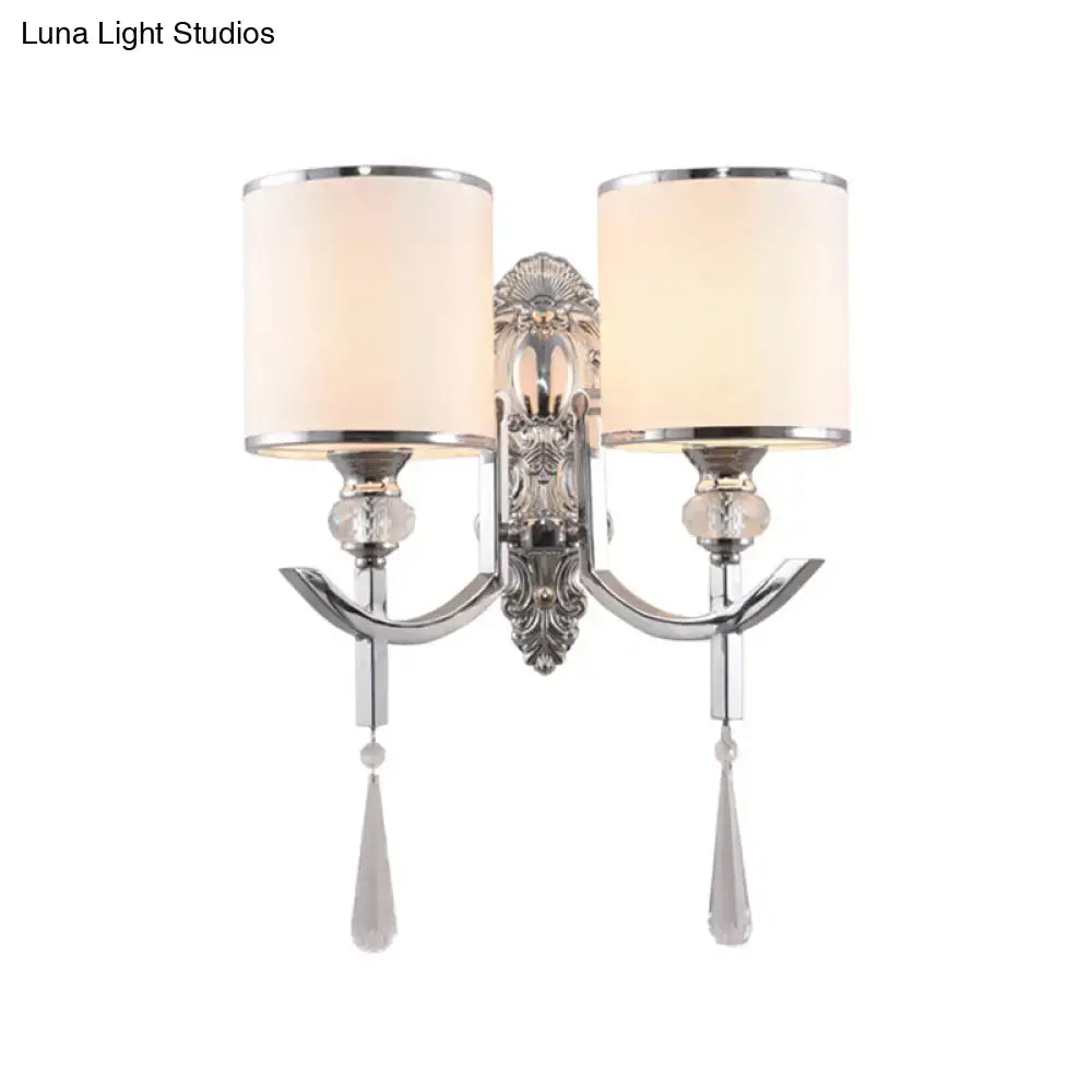 Vintage chrome wall sconce with carved backplate featuring silver ornate design, two cream fabric shades, and crystal droplets