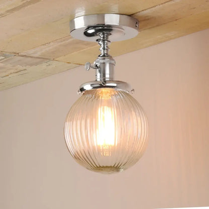 Vintage dark bronze semi flush mount ceiling light with ribbed glass globe and chrome metal fixture emitting warm glow