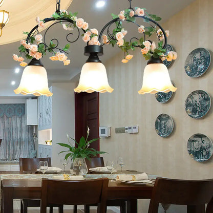 Black wrought iron chandelier with three frosted white glass shades and decorative pink roses for rose restaurant suspension