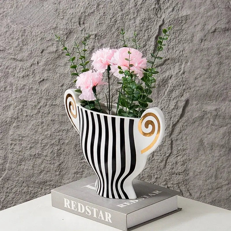 White ceramic vase with black vertical stripes and gold spiral handles holding pink carnations decorbites geometric fringe