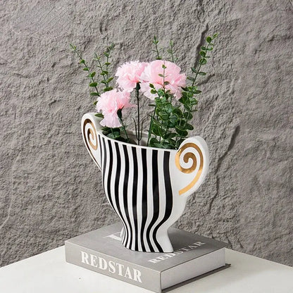 White ceramic vase with black vertical stripes and gold spiral handles holding pink carnations decorbites geometric fringe