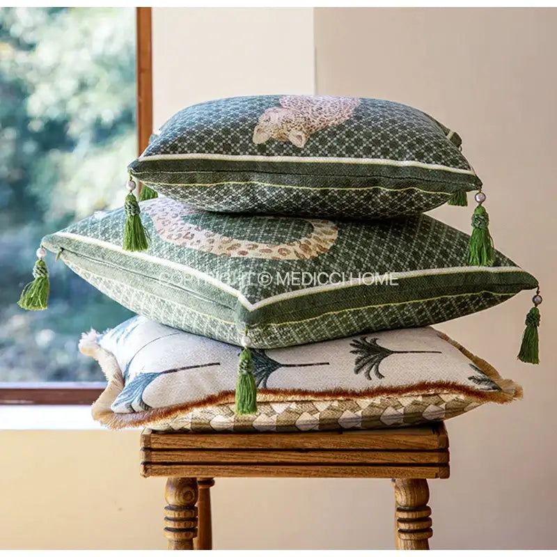 Stacked green patterned bolster pillow cases with tassel trim and embroidered leopard motifs for bedroom decor
