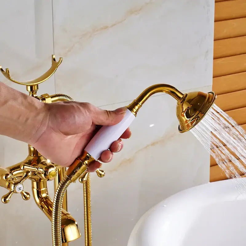 Vintage gold bath mixer tap with gold-finished handheld showerhead, white ceramic handle, and ornate brass faucet assembly