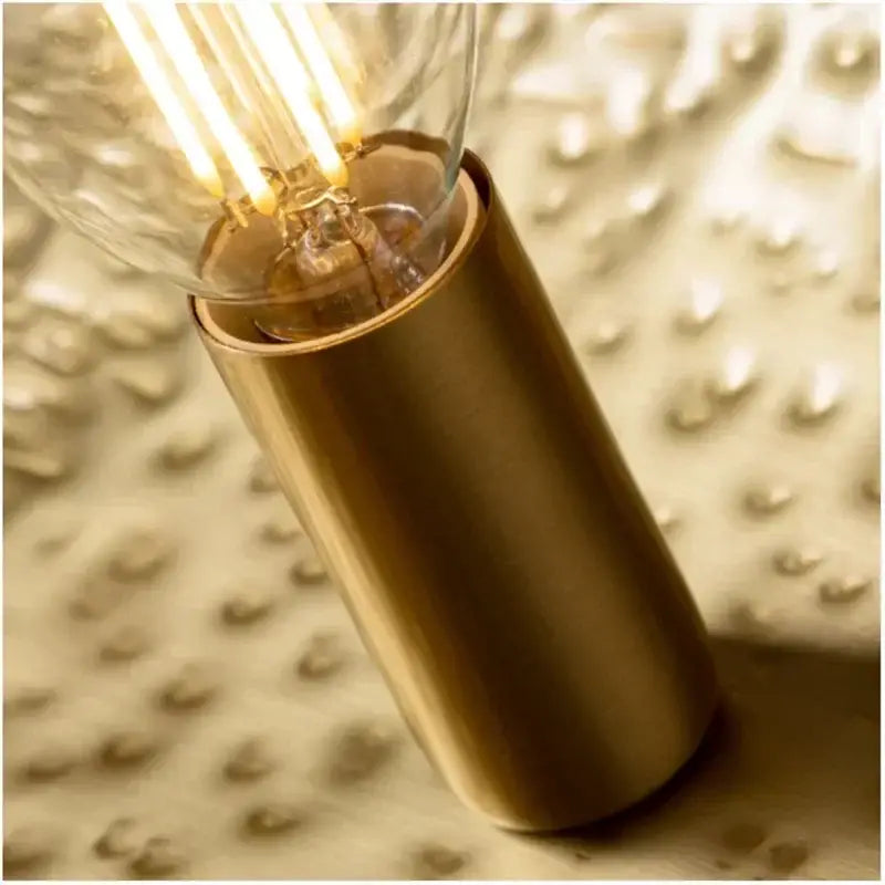 A warm glowing edison-style bulb with visible filament on a gold metal pendant light with hammered leaf design