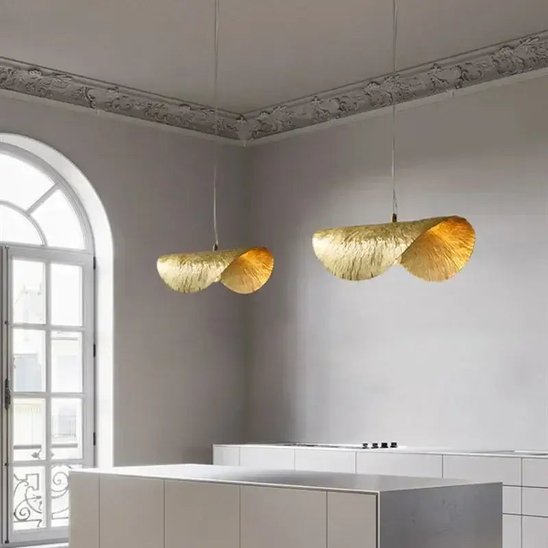 Two elegant vintage gold metal pendant lights with a hammered leaf design hang in a dining room setting