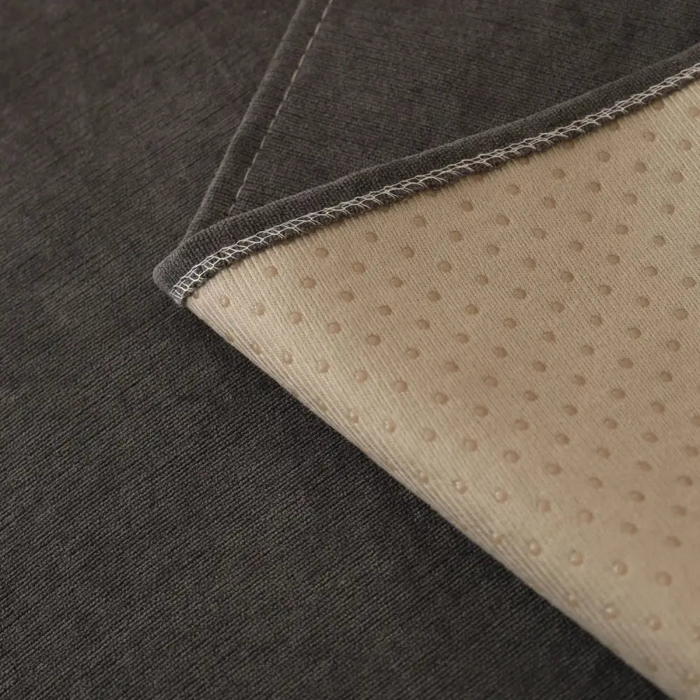 Dark gray textured fabric mat showing the beige dotted non-slip backing with white edge stitching for sofa cover use