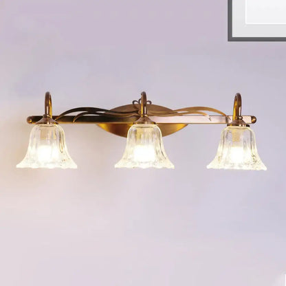 Vintage style wall light with brass finish and three clear bell-shaped glass shades for bathroom vanity use