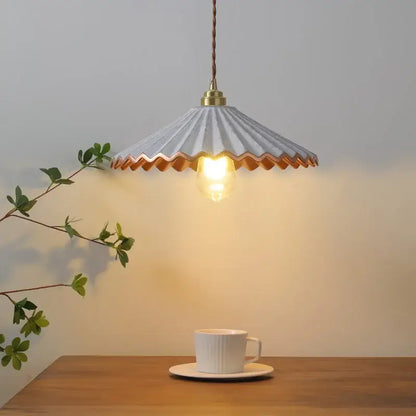 A delicate light gray decorbites ceramic led pendant light with scalloped edge and copper trim above wooden table