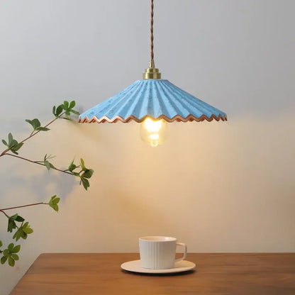 A delicate light blue scalloped ceramic led pendant light with brass fixture and twisted cord above a wooden table