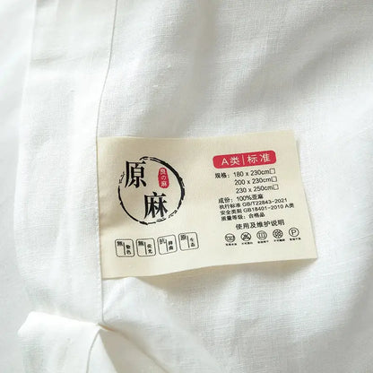 Beige fabric care label on vintage white and gray linen bedding set indicating 100 percent hemp material