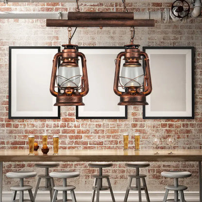 Two vintage-style copper lanterns with clear glass and intricate metalwork hang from rustic wooden beam in kitchen fixture