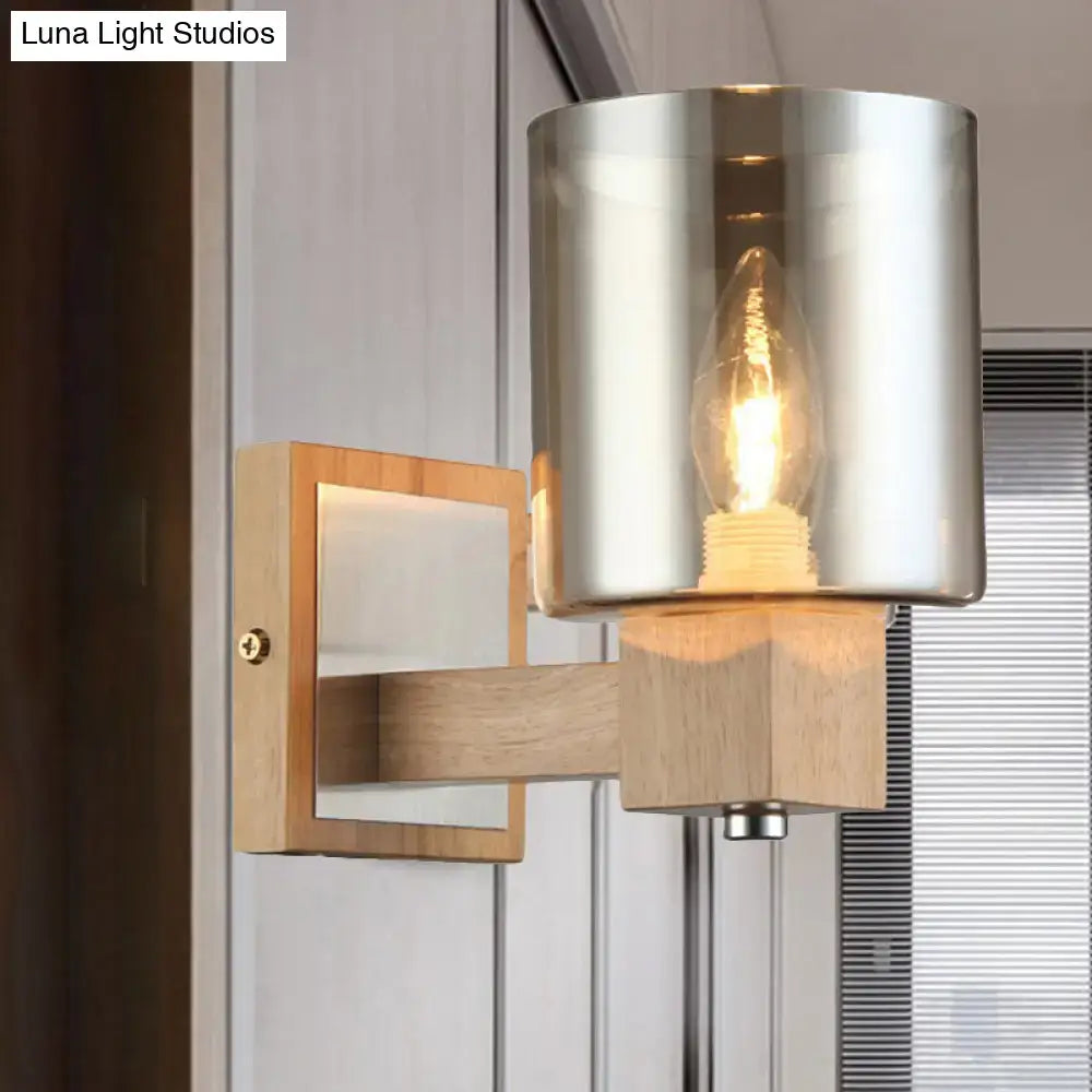 Modern wall lamp with a glass shade, brushed metallic cylindrical shade, and light wood wall mount for bedroom use