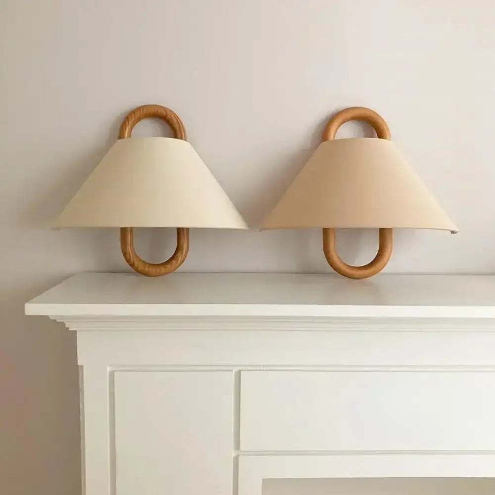 Beige fabric shades on a wabi-sabi beech wood wall lamp mounted with light wood ring fixtures for bedroom use