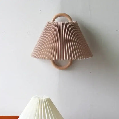Wabi-sabi beech wood wall lamp with soft blush pink pleated fabric shade and circular wooden handle mounted on white wall