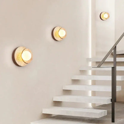 Gold-toned circular wall lamp with textured stone-like finish and warm light for decorbites cream style bedroom decor