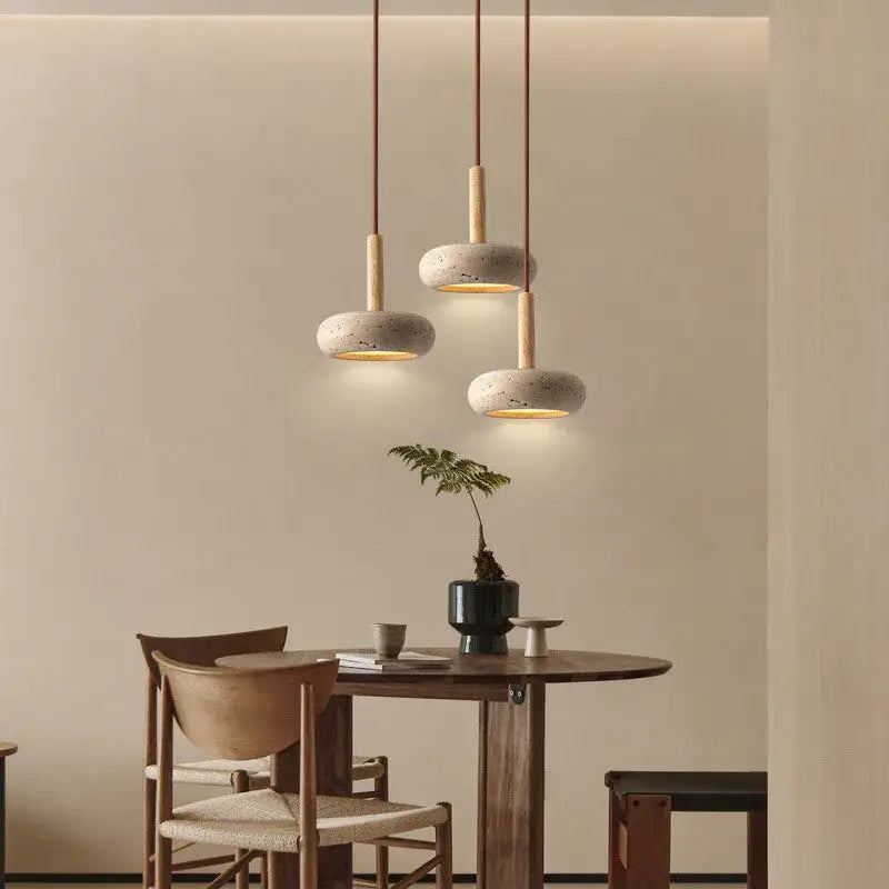 Three pendant lights with off-white concrete shades and solid wood accents hang above a dining table