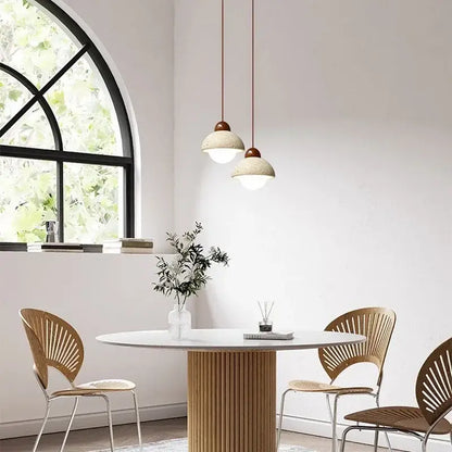 Two off-white textured ceramic cave stone pendant lights with copper fixtures hang in a dining room decorbites cave stone decor