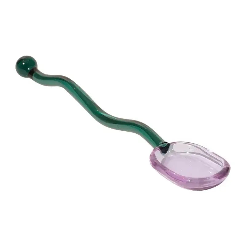 A translucent purple glass spoon coffee stirring rod with a curved emerald green handle in wavy colorful kitchen set
