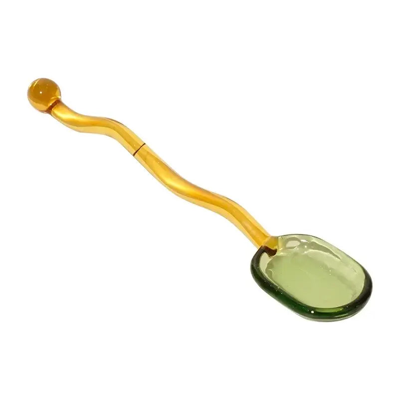 A translucent amber glass spoon coffee stirring rod with a wavy handle and green-edged oval bowl for kitchen use