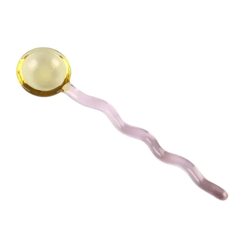 A translucent yellow glass spoon coffee stirring rod with a wavy pale pink handle for kitchen use