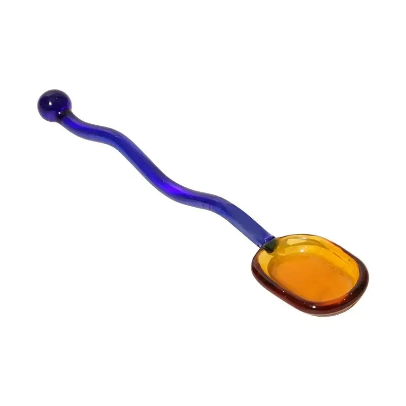 A vibrant wavy colorful glass spoon coffee stirring rod with cobalt blue handle and amber irregular bowl for kitchen use