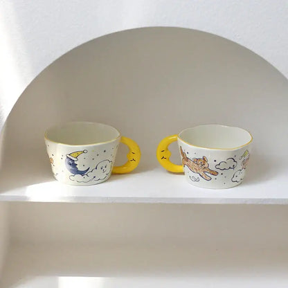 Two whimsical off-white bear moon ceramic mugs with yellow handles and hand-painted moon and cat illustrations
