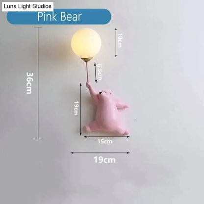 Whimsical pink polka dot girl wall lamp with a matte pink bear holding a frosted glass bulb on a slender metallic stem