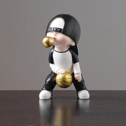 A black and white whimsical resin boys sports statue holding a gold basketball and blowing a golden bubble gum ball